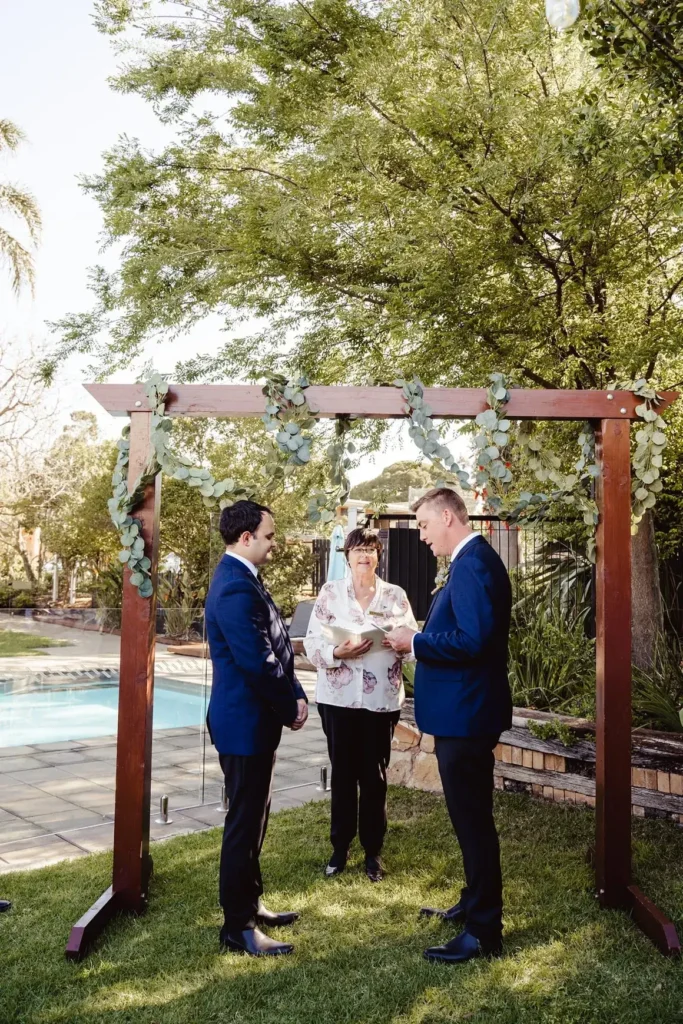 Outdoor wedding ceremony under decorated wooden arch.