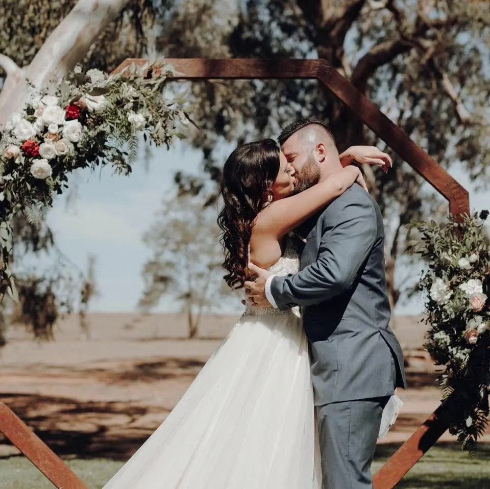 Bride and groom kissing under floral arch.